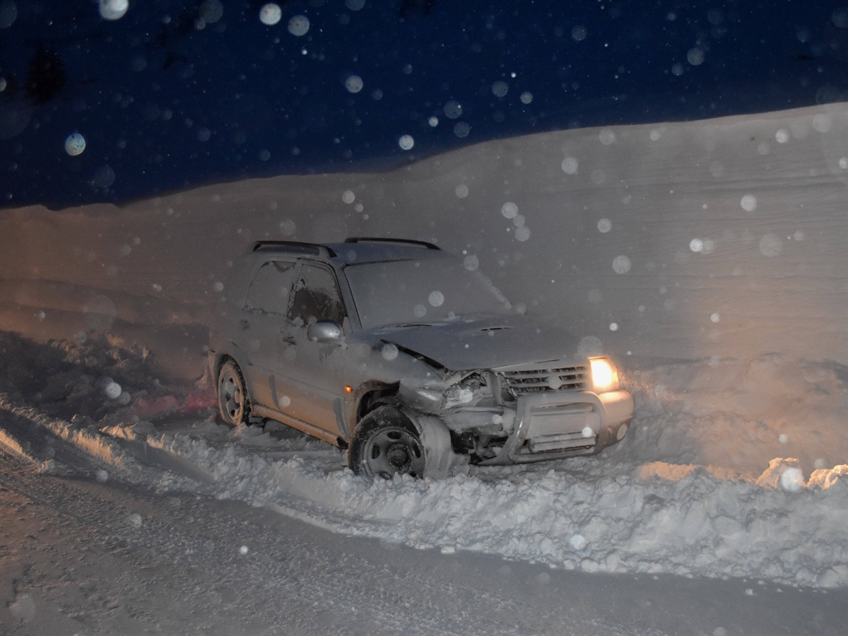 Bild in fortgeschrittener Abenddämmerung. An einer Schneewand von schräg vorne ein stark beschädigtes Auto. 