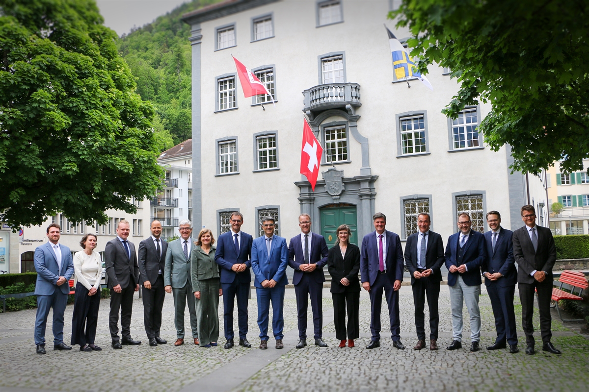 Die Bündner und die Vorarlberger Delegation vor dem Regierungsgebäude mit den beiden Flaggen im Hintergrund