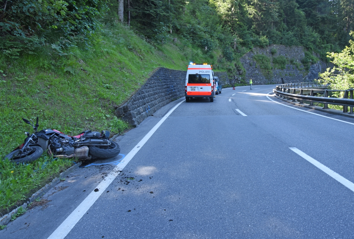 Motorrad liegt am Fahrbahnrand auf der Seite. Im Hintergrund der Unfallwagen der Kantonspolizei Graubünden