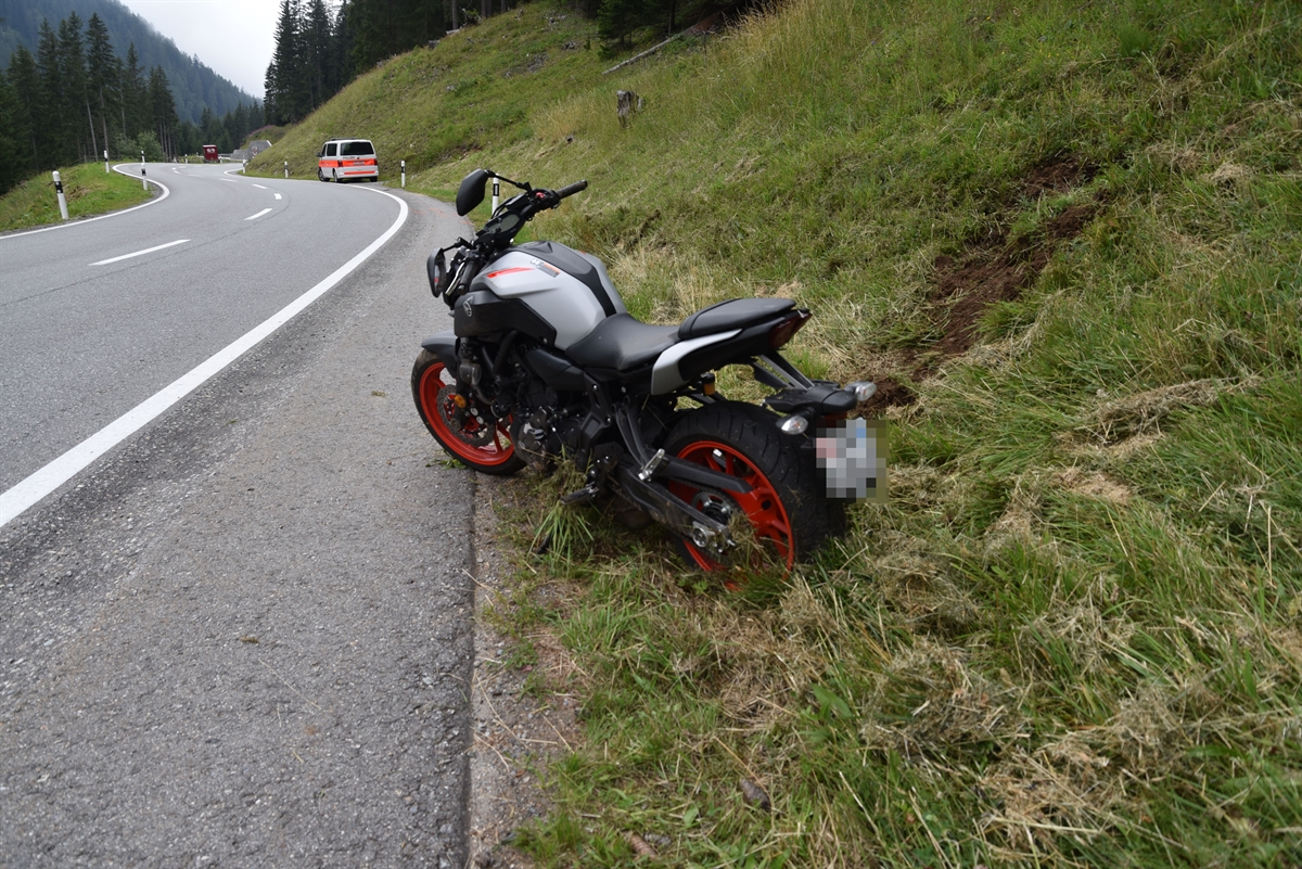 Leichtbeschädigtes Motorrad stehend im Wiesland neben der Strasse. Im Hintergrund das Polizeifahrzeug.
