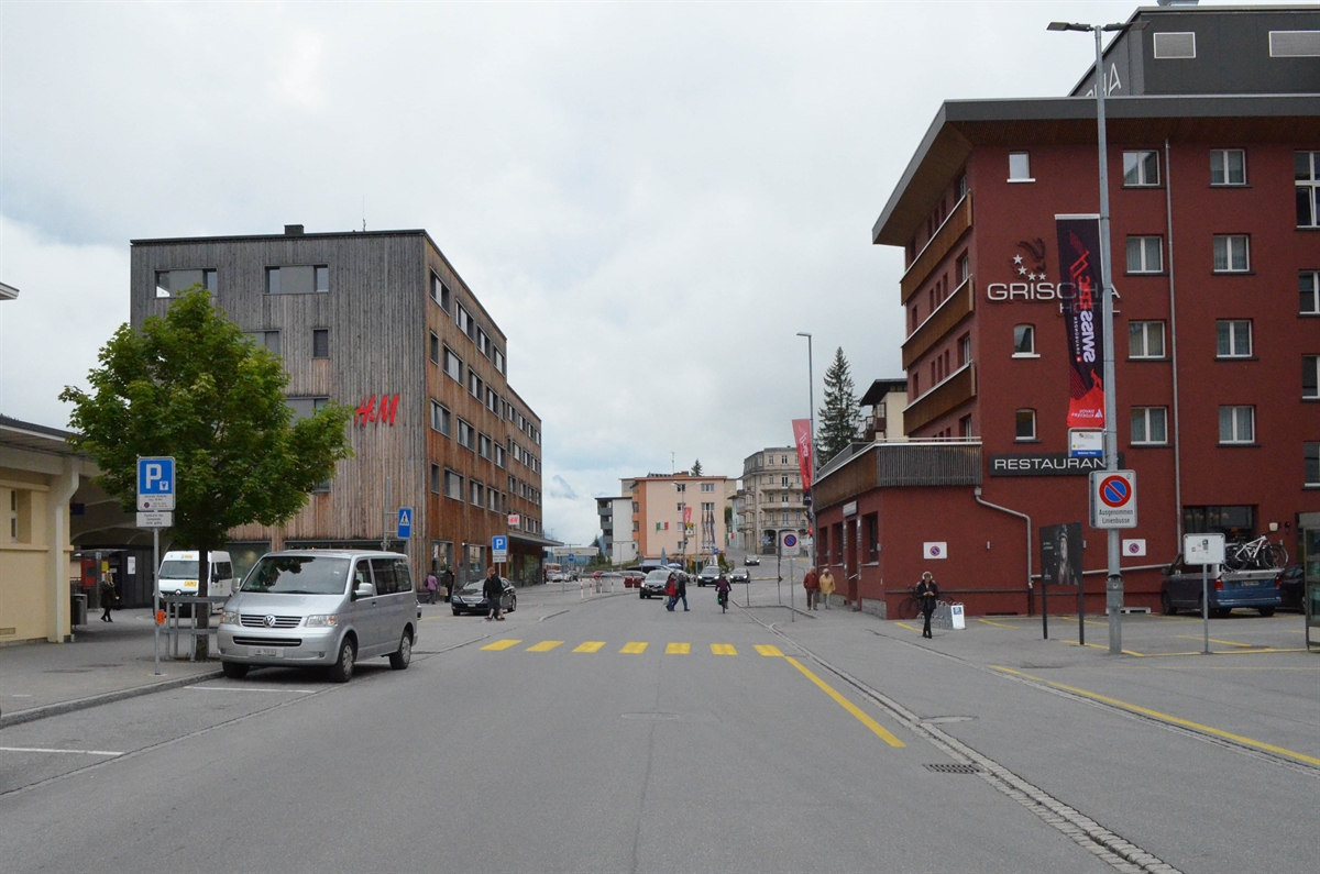 Die Strasse in Blickrichtung Spital mit dem Fussgängerstreifen. Links ein Teil des Bahnhofgebäudes und rechts das Hotel Grischa.
