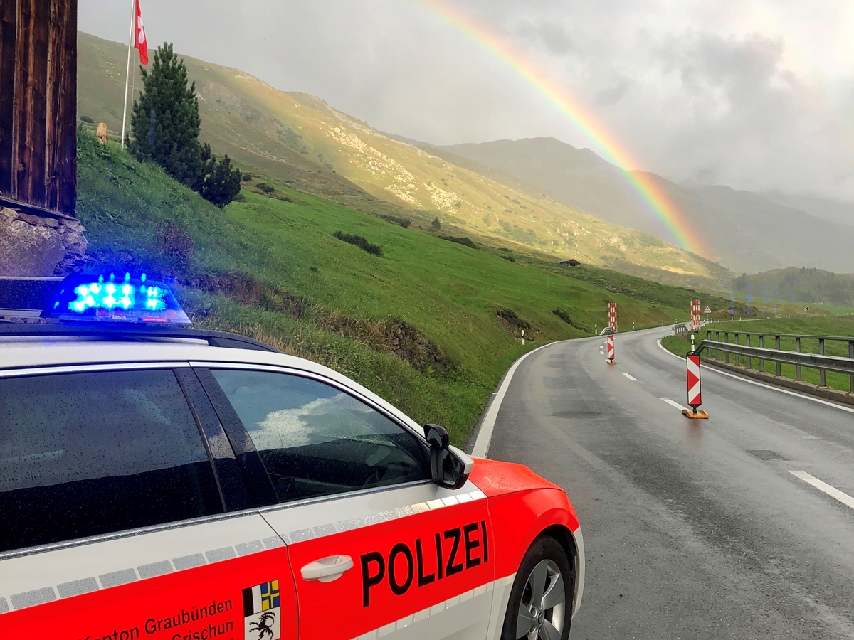Örtlichkeit, bei welcher der Motorradlenker angehalten hat. Patrouillenfahrzeug der Kantonspolizei Graubünden mit Strassenverlauf in Richtung Flüela Hospiz. Im Hintergrund ein Regenbogen.