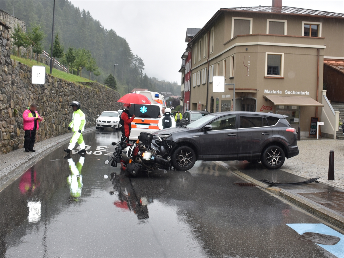 Die Unfallstelle mit dem aus dem Parkplatz fahrenden Auto. Seitlich vor dem Auto liegt das Motorrad. Im Hintergrund steht das Ambulanzfahrzeug.