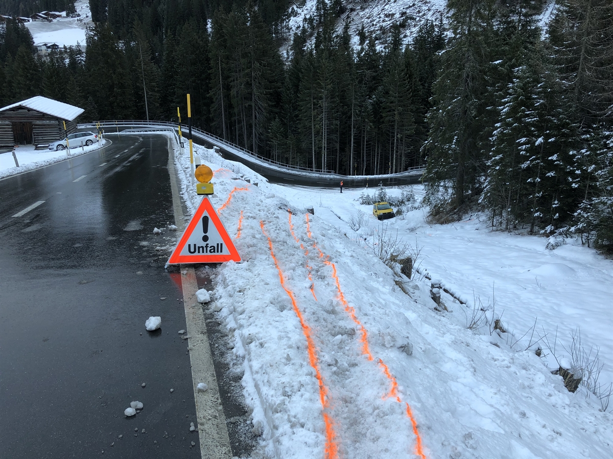 Eingezeichnete Spuren im Schnee mit Fahrzeugwrack am Ende des Abhangs.