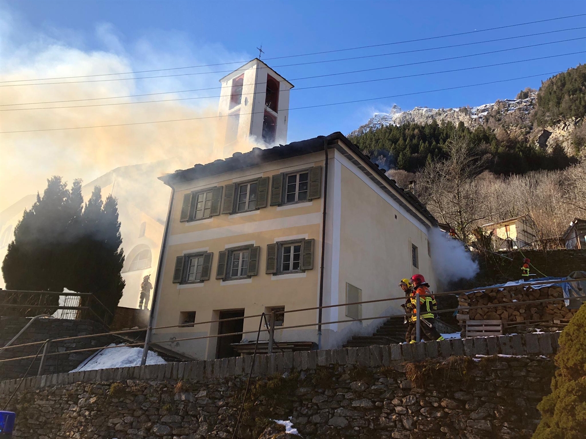 Brennendes Haus neben der Kirche und Feuerwehrleute im Einsatz
