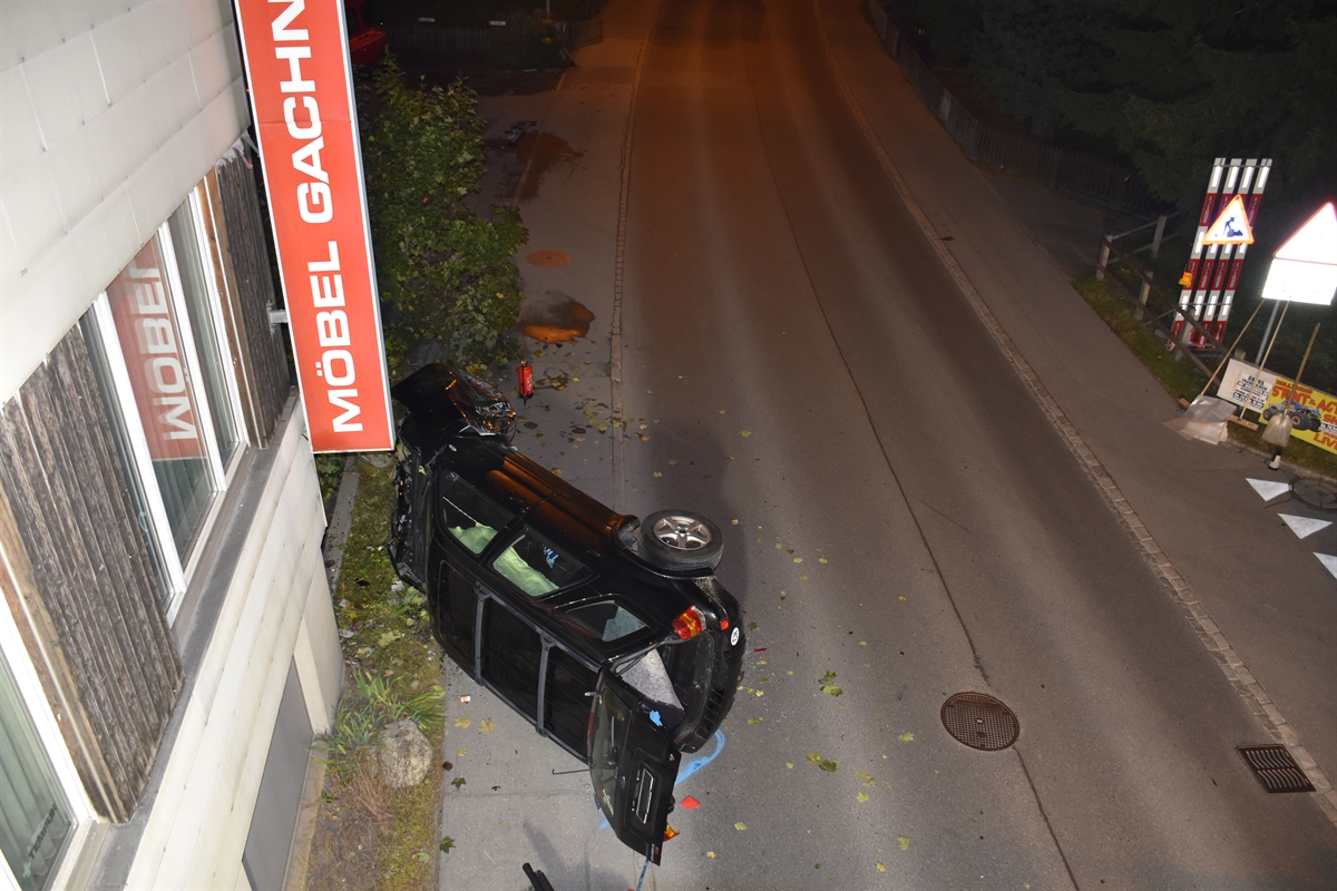 Übersichtliche Kurve und beschädigte Signale.  Auto liegt an einem Gebäude in Seitenlage auf Trottoir. 