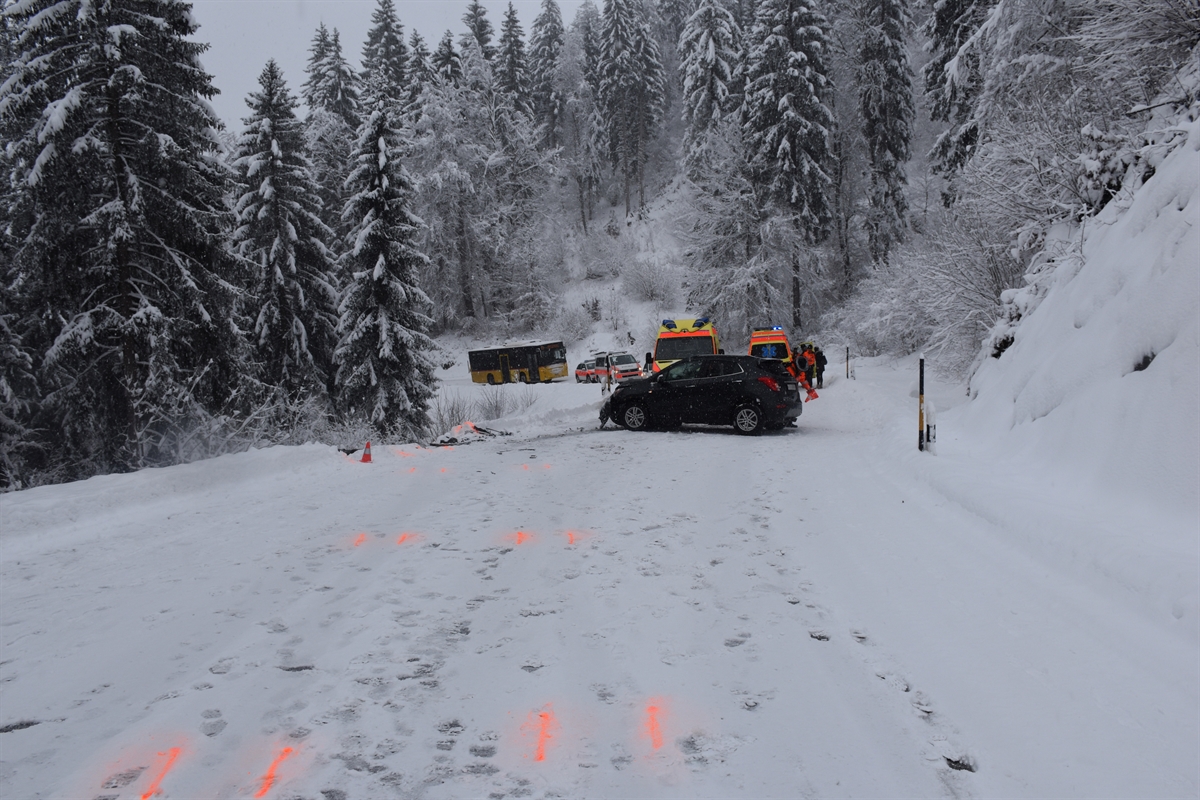Das bergwärts fahrende Auto quer auf der schneebedeckten Strasse. Im Hintergrund davon zwei Ambulanzen, zwei Polizeiautos und ein Postauto.