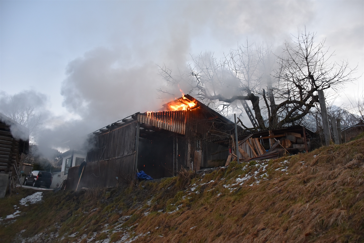Ansteigende Wiesenböschung, oberhalb davon die Remise. Aus deren Dach sind Flammen ersichtlich. Links davon ein Einfamilienhaus.
