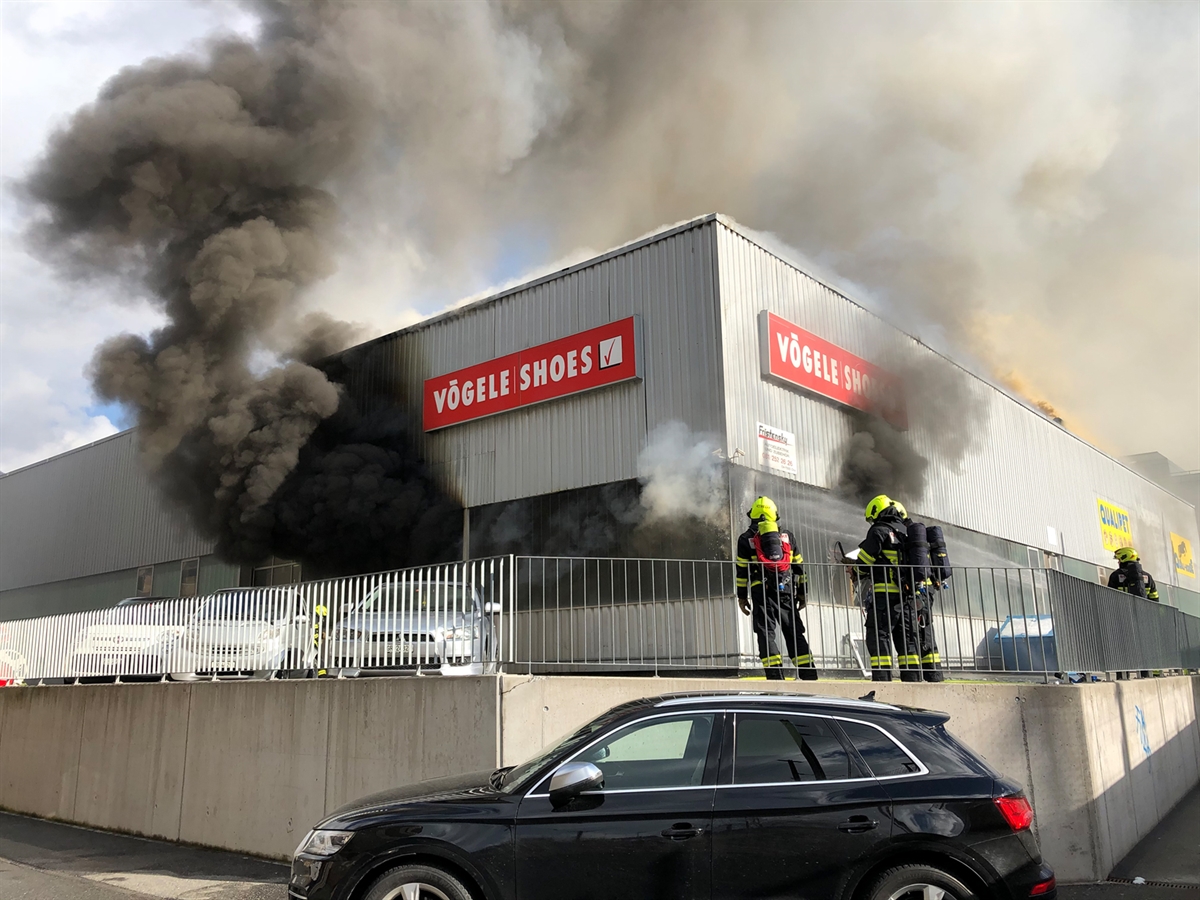 Das Geschäftsgebäude mit starkem Rauch aus dem Pneulager. Feuerwehrleute bekämpfen den Brand