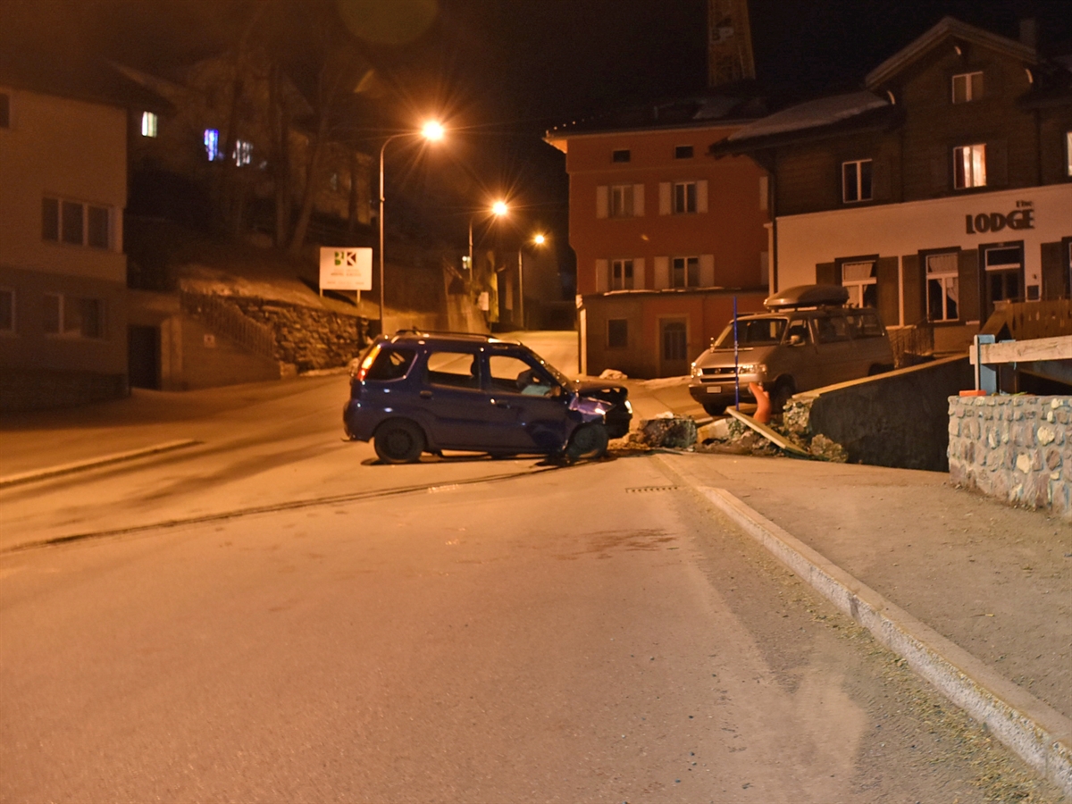 Das total beschädigte Unfallfahrzeug quer auf der Bergspur in Richtung Lenzerheide. Rechtsseitig eine zum Teil vollständig zerstörte Mauer mit einem Personenwagen im Hintergrund vor einem Haus.