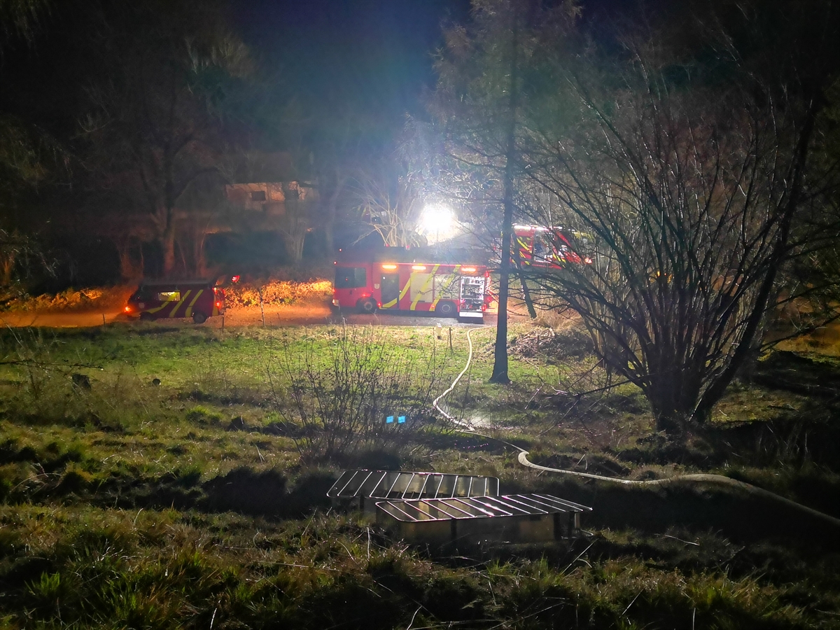 Drei beleuchtete Feuerwehrfahrzeuge in der Nacht von Tamins. Eine Druckleitung ist am Hang erstellt.
