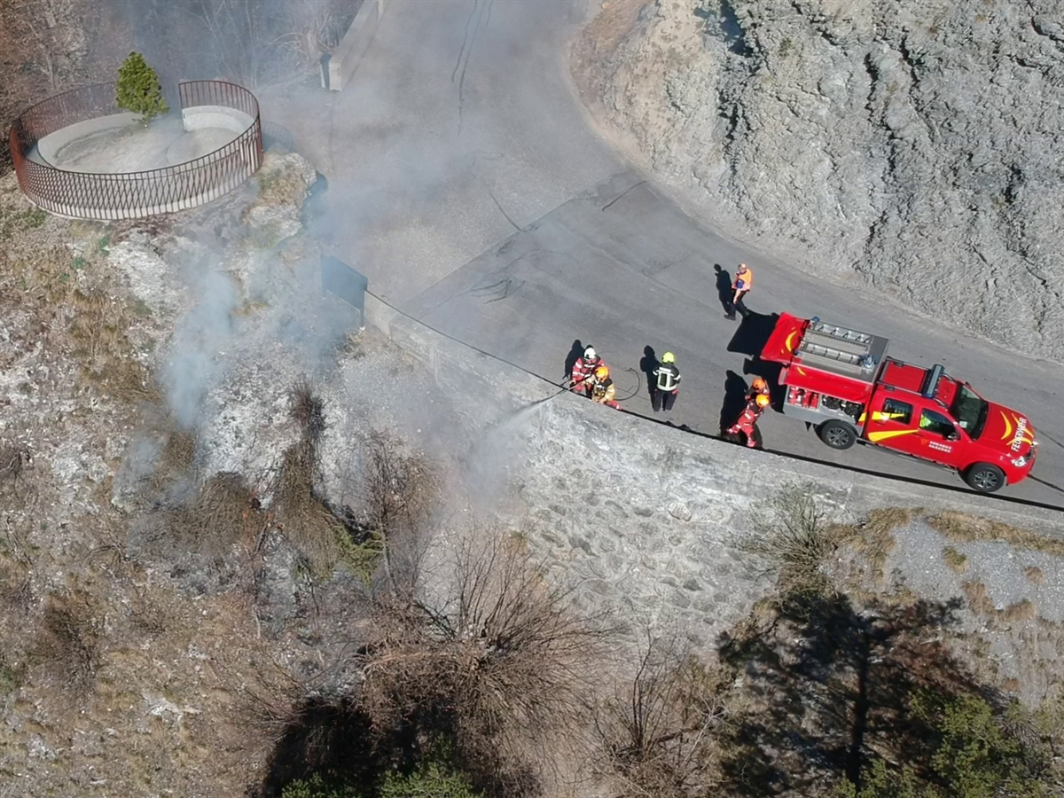 Auf der rechtsrheinischen Oberländerstrasse steht ein Feuerwehrauto. Ein Feuerwehrmann spritzt Wasser über die Stützmauer in das Tobel hinunter. Weitere Feuerwehrleute springen dem Mann zu Hilfe.