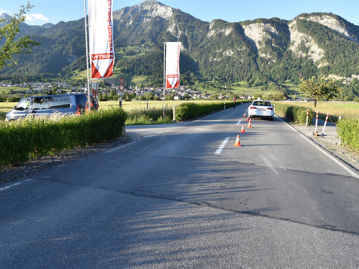 Malanserstrasse mit dem auf der rechten Fahrspur stehenden weissen Auto. Links und rechts wird die Strasse durch eine Hecke begrenzt. Links die Einfahrt zum Feldweg