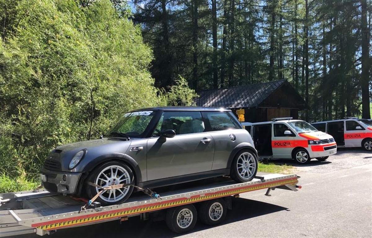 Personenwagen auf Anhänger aufgeladen und gesichert. Im Hintergrund zwei Polizeifahrzeuge.