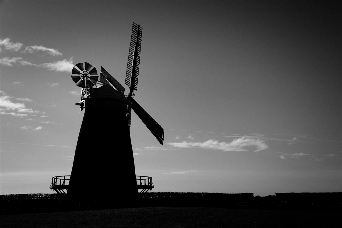 Ein düsteres schwarzweisses Landschaftsbild. Die oberen zwei Drittel ausgefüllt mit Horizont. Links im Bild eine Windmühle.