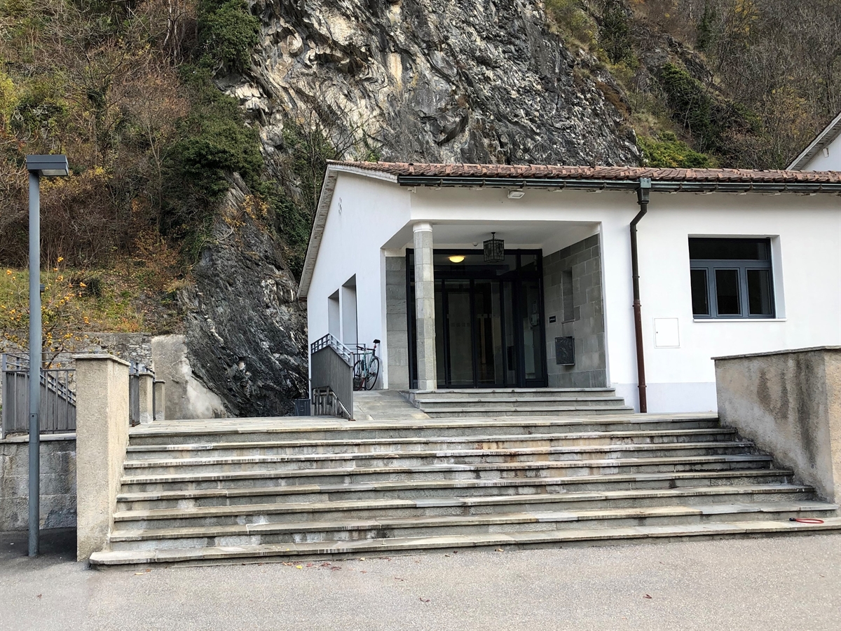 Treppen die zum Gebäudeeingang hochführen. Teilaufnahme des Gebäudes. Im Hintergrund eine Felswand.