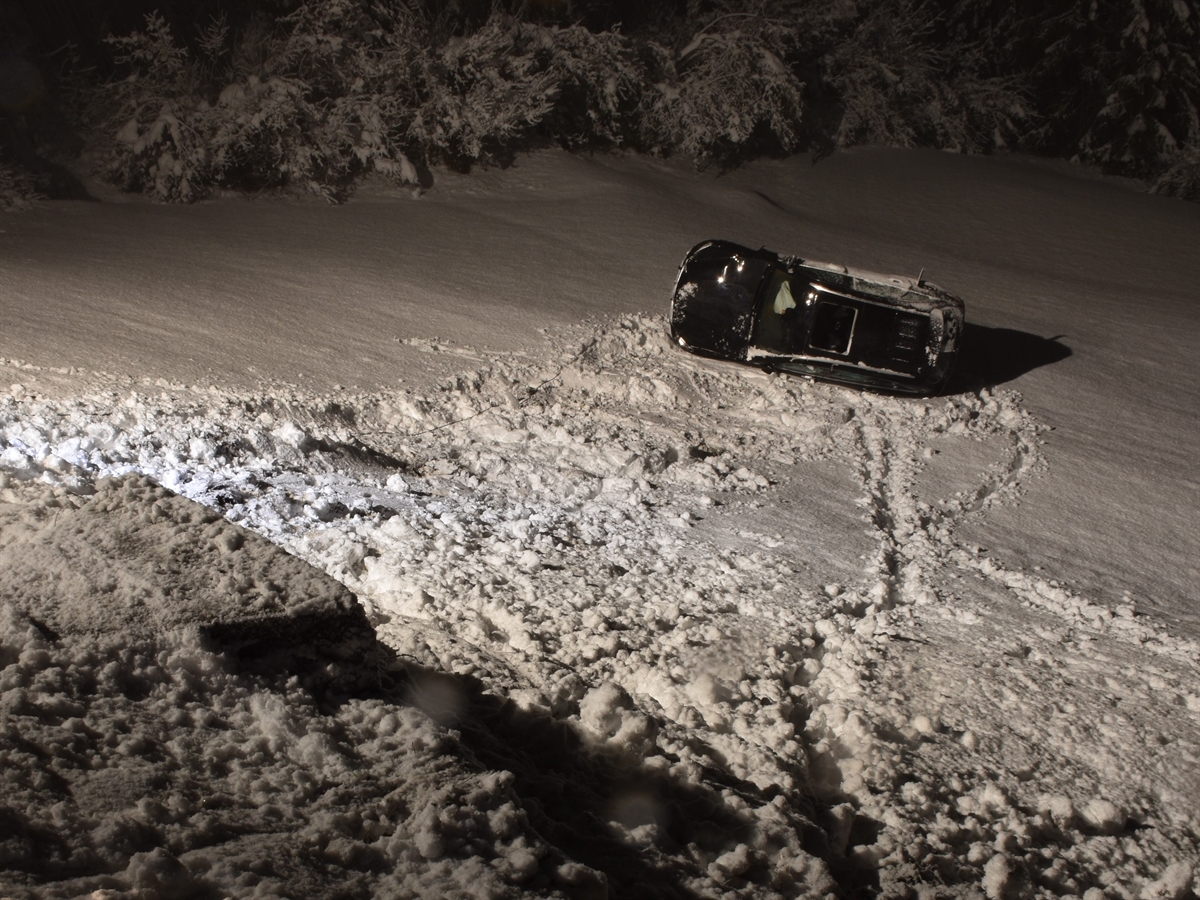 Nachtaufnahme, von schräg oben das in der Böschung auf der Fahrerseite liegende Auto. Alles ist schneebedeckt. 