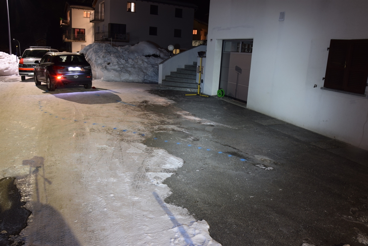 Vor dem Wohnhaus mit der Garageneinfahrt steht das Auto auf dem schneebedeckten Vorplatz. Im Hintergrund ein Patrouillenfahrzeug der Kantonspolizei Graubünden.