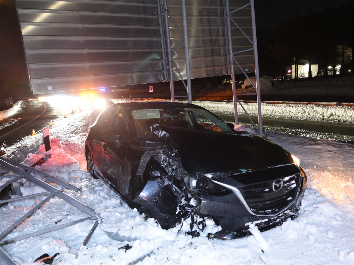 Nachtaufnahme, frontal im Vordergrund das auf der Beifahrerseite beschädigte Auto im Schnee. Unmittelbar dahinter die mehrere Meter breite Signalisation, deren Stützen zum Teil demoliert im Schnee liegen.