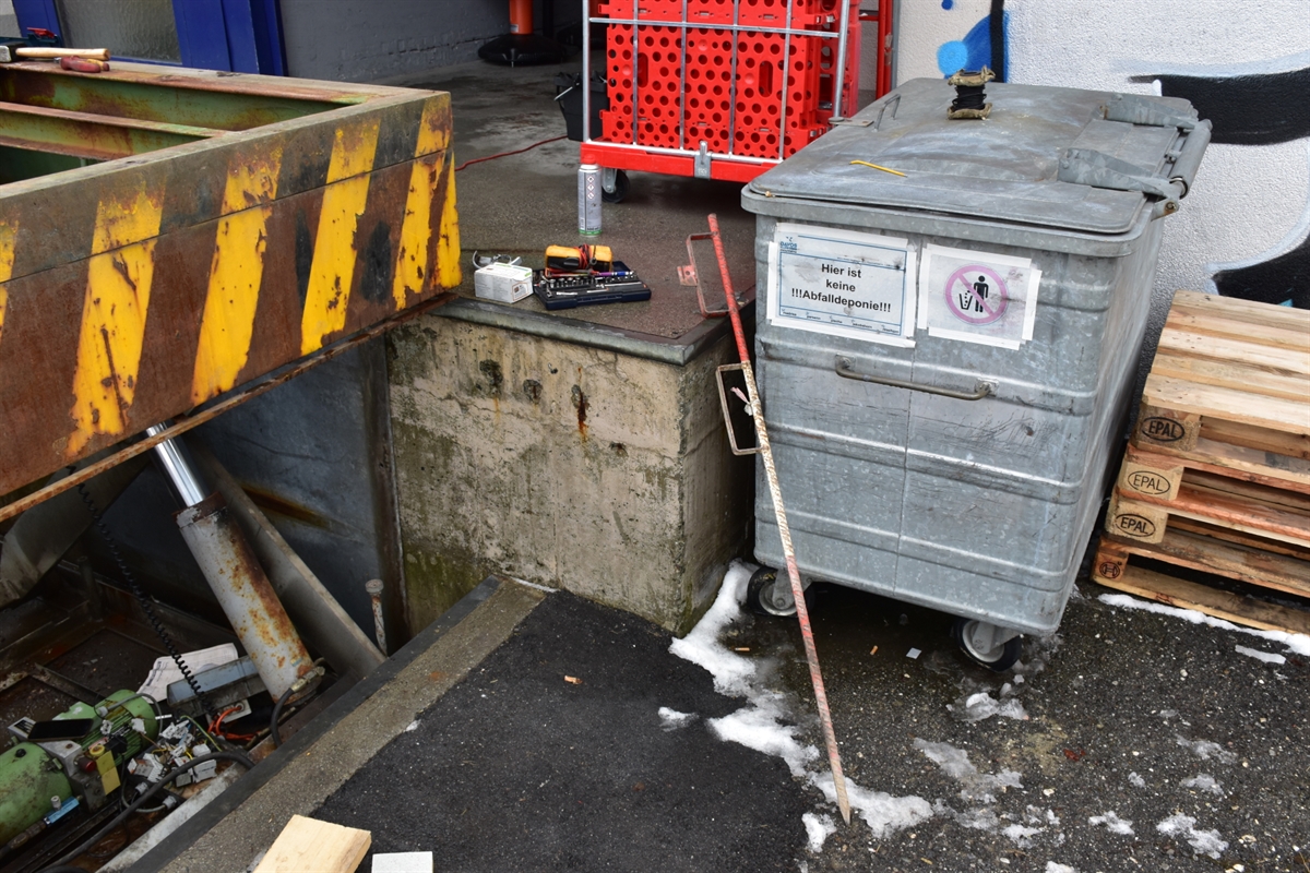 Links die hochgefahrene Heberampe. Neben der Rampe steht ein Abfallcontainer sowie auf der angrenzenden Betonrampe verschiedenes Werkzeug.