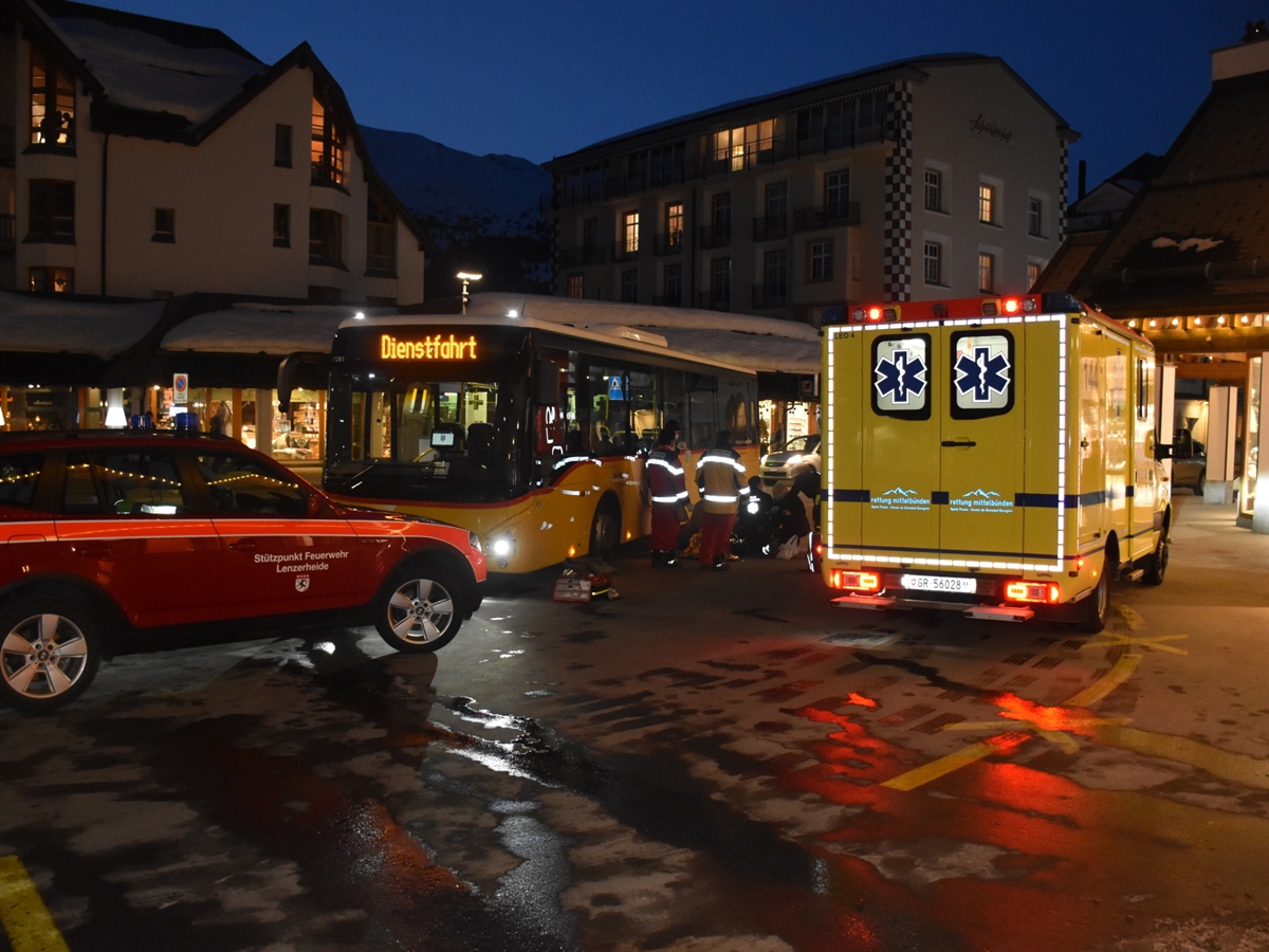 Postplatz in Lenzerheide. Mitten im Bild wird neben dem Postauto die Frau durch die Rettung betreut. Im Vordergrund ein Einsatzfahrzeug der Feuerwehr und ein Ambulanzfahrzeug.