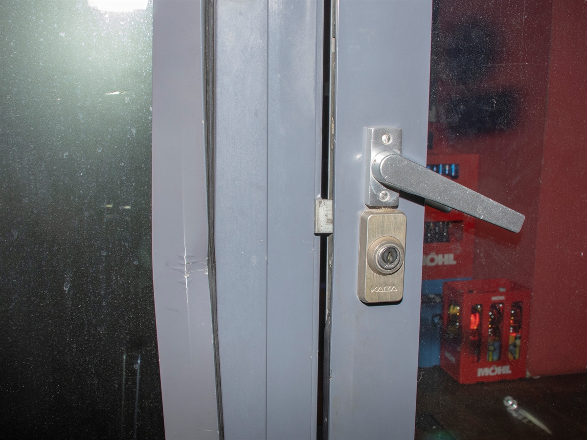 Eine aufgebrochene Metalltüre, die Spuren von Einbruchwerkzeug sind gut erkennbar. Im Hintergrund Getränkeharasse in einem Innenraum.