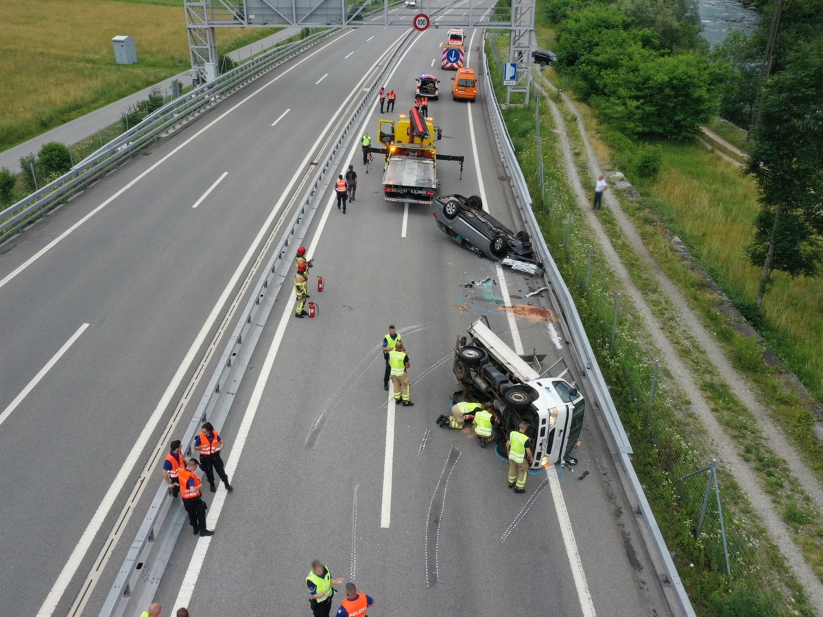 Die Unfallstelle auf der Autobahn A13 mit mehreren Einsatzkräften, Einsatzfahrzeugen sowie einem Abschleppwagen auf der Nordspur. Die beiden Unfallfahrzeuge im Vordergrund. Der Lieferwagen auf der Seite liegend und das Auto auf dem Dach liegend.