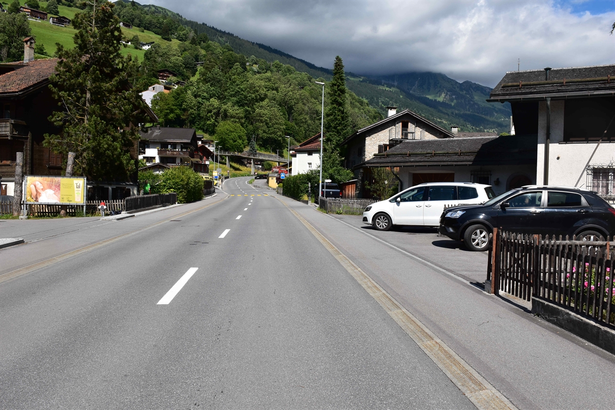 Blick in Fahrtrichtung Richtung Davos auf die Strasse. Rechtsseitig ist eine Quartiereinfahrt wo 2 Autos parkiert sind.
