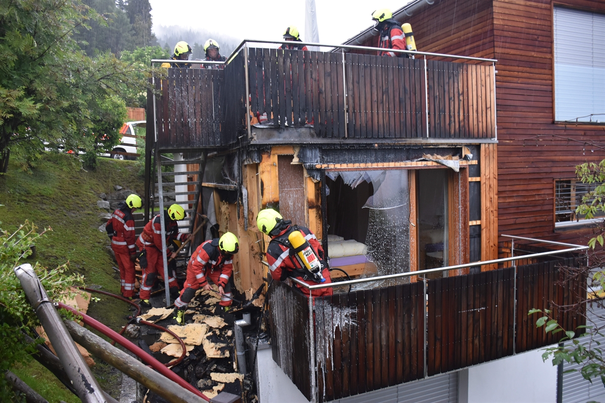 Feuerwehrleute brechen Fassadenteile des Holzhauses ab