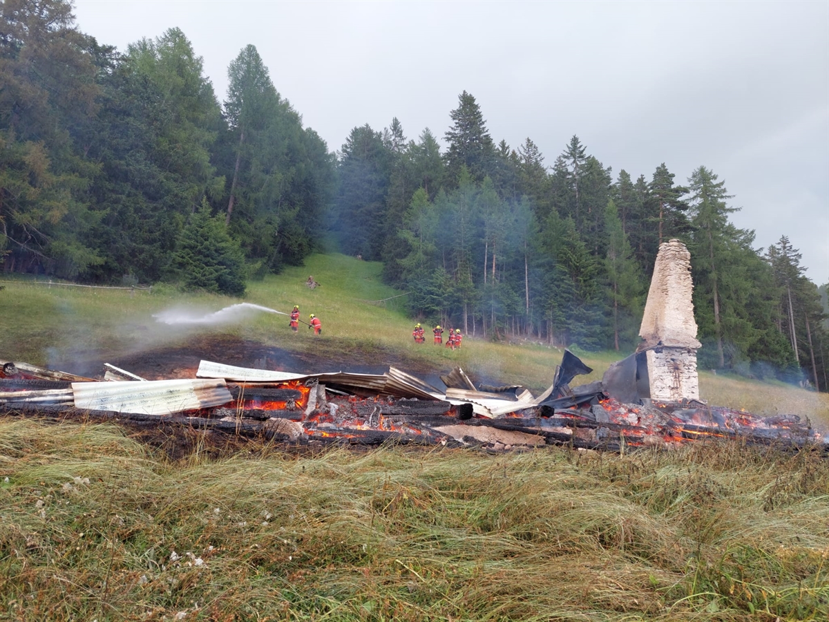 Vom Feuer zerstörtes Maiensäss mit Stall, im Hintergrund Feuerwehrleute