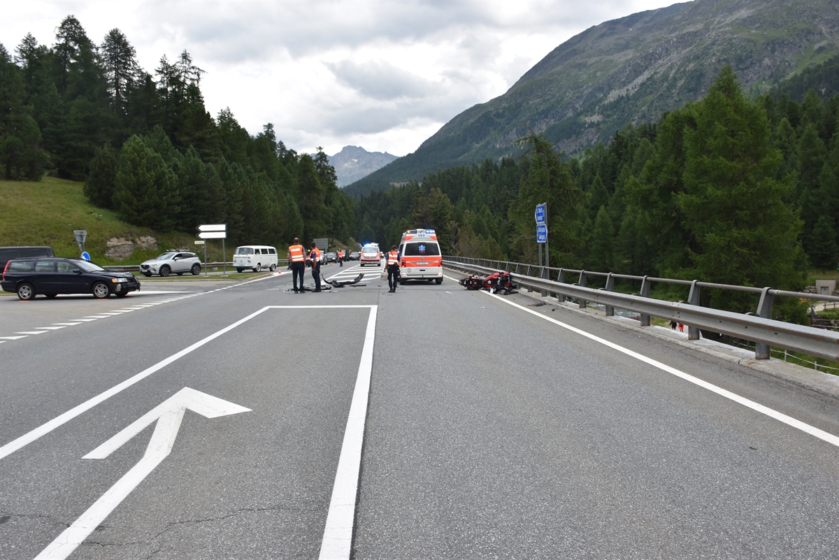 Übersicht der Unfallstelle: Linksseitig ist das Auto welches von Champfèr auf die H27 abbiegen wollte. Rechtsseitig ist das total beschädigte Motorrad. Zwischen den beiden Fahrzeugen ist ein Polizeibus mit Blaulicht zu sehen und die Ambulanz, die die Unfallstelle verlässt.