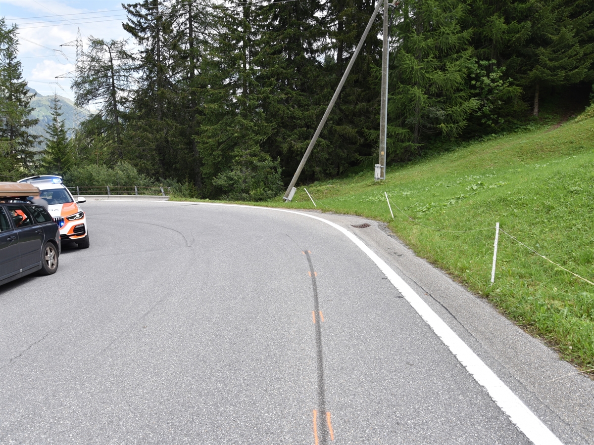 Rechtskurve der Splügenpass-Strasse. Auf dem Belag ist eine Bremsspur eines Motorrades ersichtlich, die schnurgerade auf die Kurve führt. Im Hintergrund durch die Böschung abfallende Wald sowie ein Strommast. Am linken Fahrbahnrand steht ein Patrouillenfahrzeug sowie ein Privatfahrzeug.
