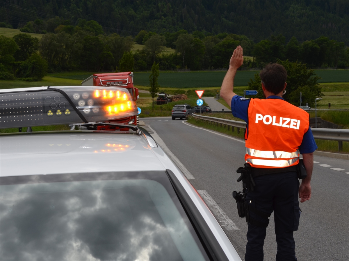 Patrouillenfahrzeug der Kantonspolizei Graubünden. Rechts daneben steht ein Polizist mit dem Rücken zum Bild und gibt für den Verkehr ein Haltezeichen.