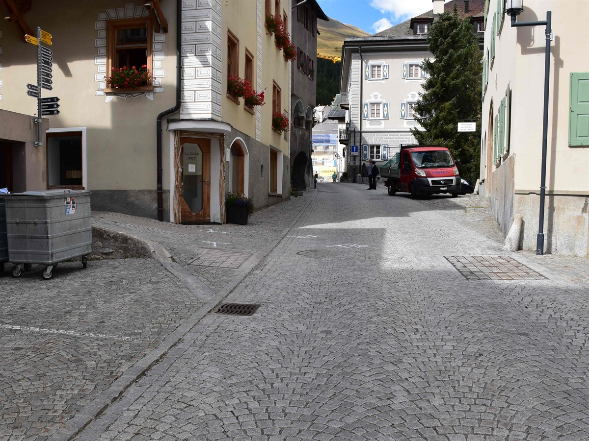 Links die Seitengasse und rechts davon die Via San Bastiaun, beide in Pflastersteinen ausgeführt. Auf der Fahrbahn weisse Markierungen der Unfallendlage des Autos. 