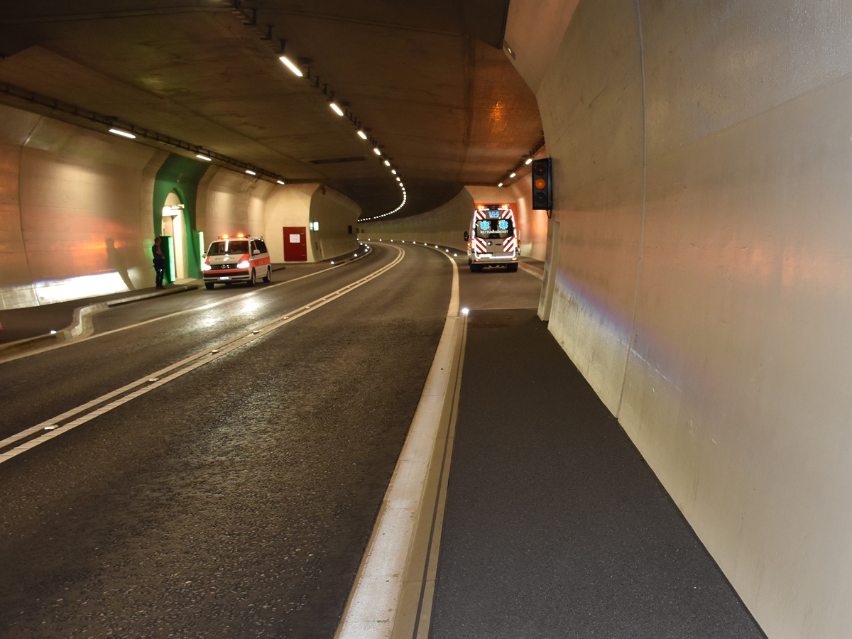 Aufnahme im Tunnel vom Trottoir in Richtung Notfallnische. In der Nische das Ambulanzfahrzeug. Rechts gegenüber, ebenfalls in einer Nische, ein Polizeiauto.