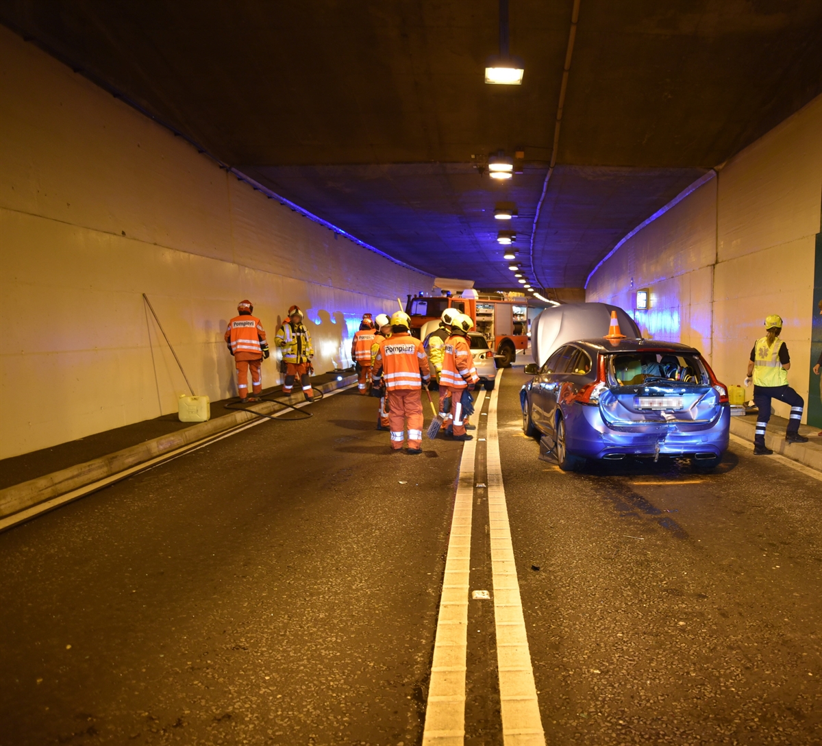 Tunnel mit den zwei beschädigten Personenwagen von hinten und im Hintergrund ein Feuerwehrfahrzeug. Diverse Feuerwehrleute und die von der Rettung im Einsatz.