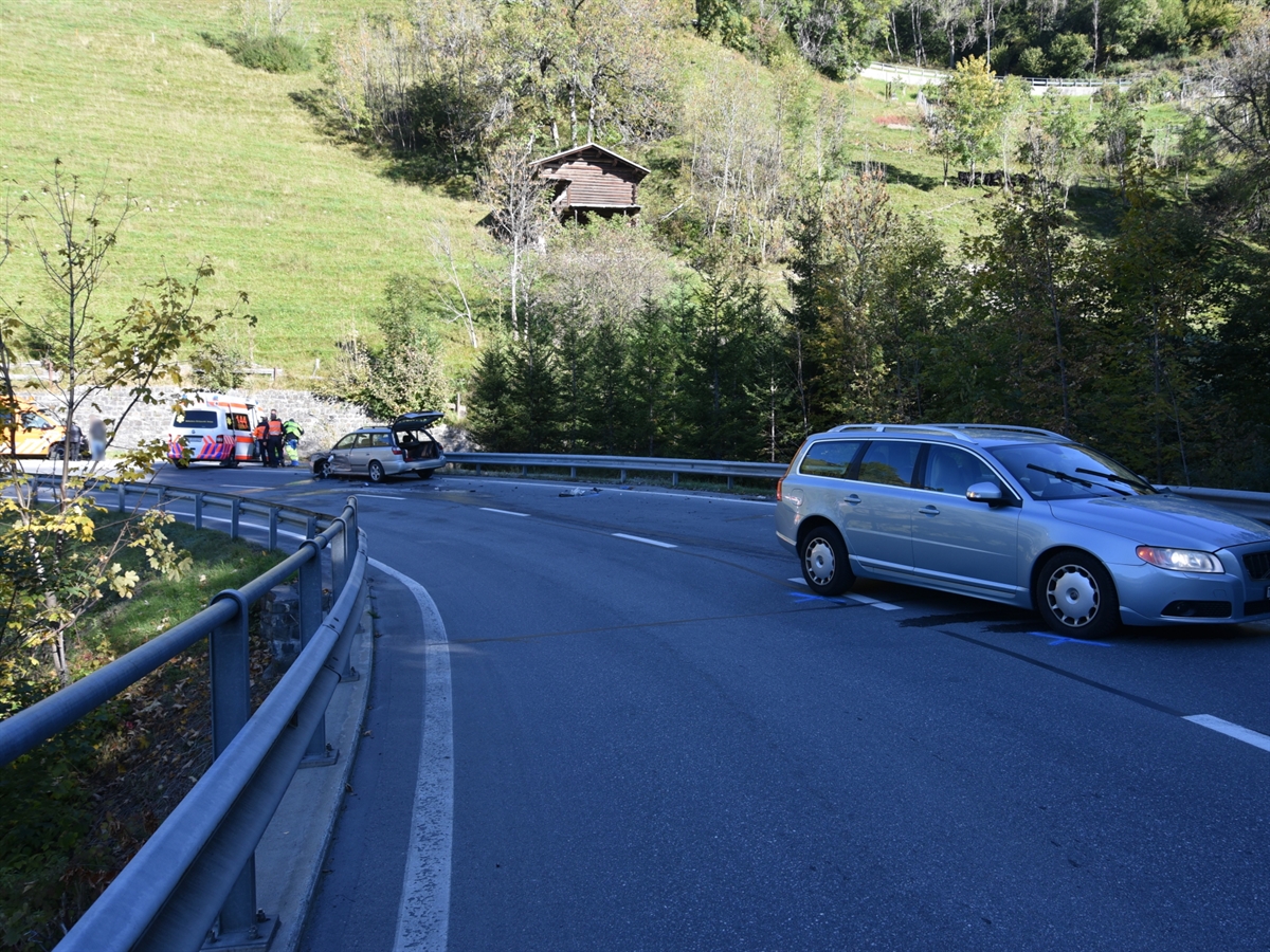 Am rechten Bildrand steht das Auto der bergwärts fahrenden Automobilistin. Am linken Bildrand das talwärts fahrende Auto. Links davon steht ein Ambulanzfahrzeug sowie ein Fahrzeug des Tiefbauamt Graubünden.