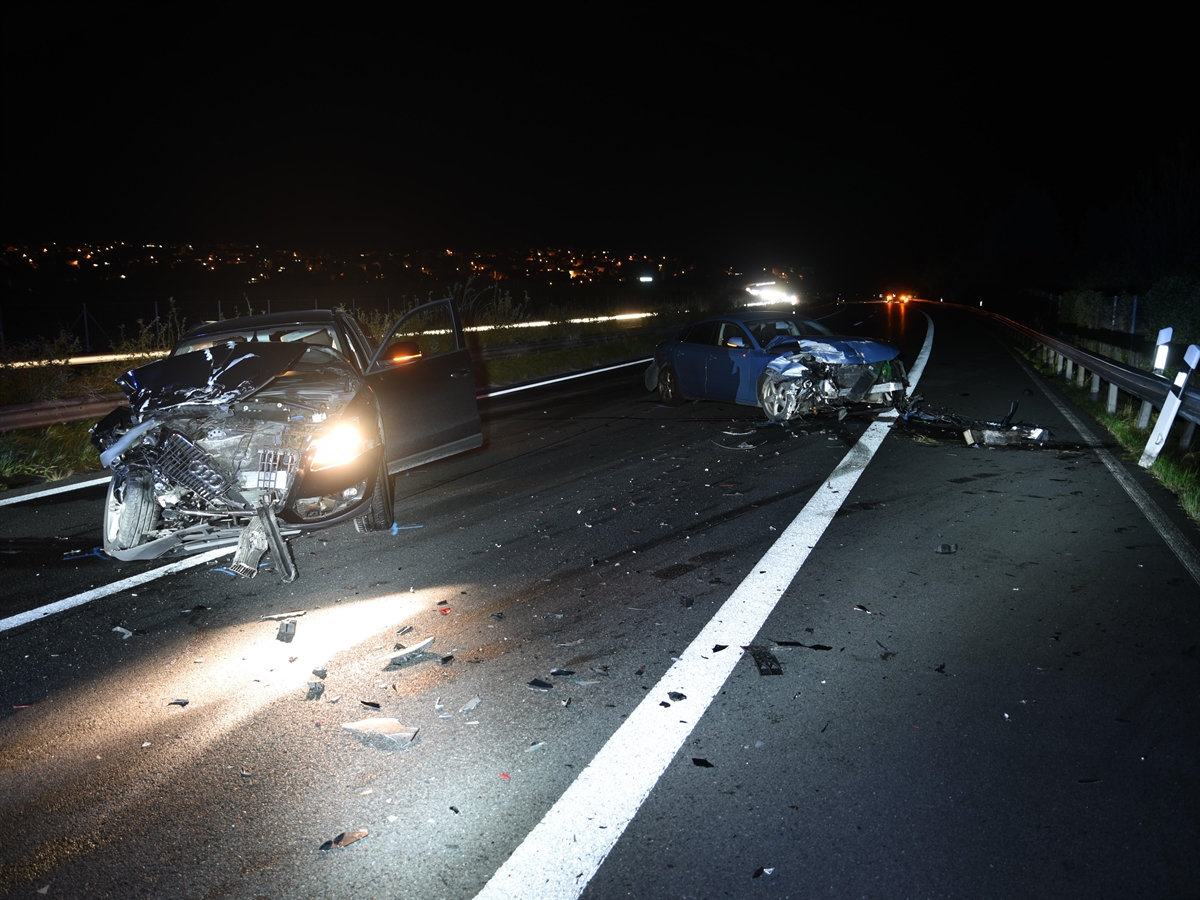 Eine Aufnahme im Dunkeln mit den beiden total beschädigten Autos. Links ein dunkler Wagen, rechts davon ein hellblauer. Beide stehen schräg entgegen der ursprünglichen Fahrtrichtung auf der Autobahn.