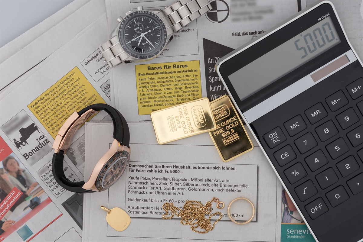Zeitungsinserate auf welchen zwei Goldvreneli, zwei wertvolle Uhren, weiterer Goldschmuck sowie ein Taschenrechner liegen.