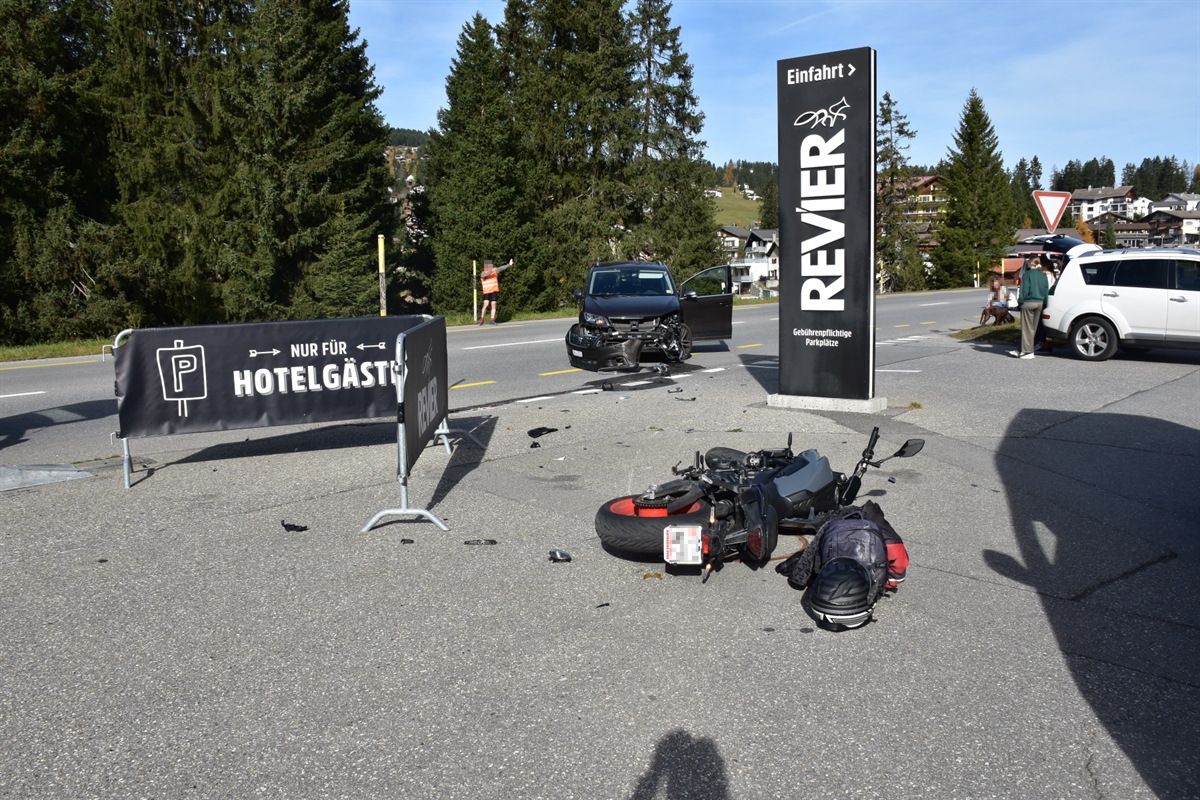 Einfahrt Parkplatz Bergbahnen Lenzerheide: Im Vordergrund liegt das beschädigte Motorrad in der Einfahrt und im Hintergrund steht der beschädigte Pw quer auf der Fahrbahn.