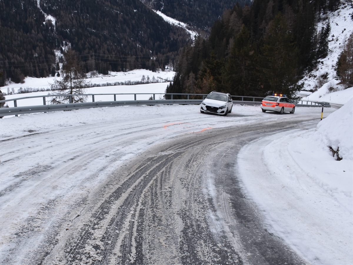 Die schneebedeckte Unfallkurve von oben her gesehen. Mittendrin ein weisses frontal beschädigtes Auto, rechts davon ein Polizeiauto. 
