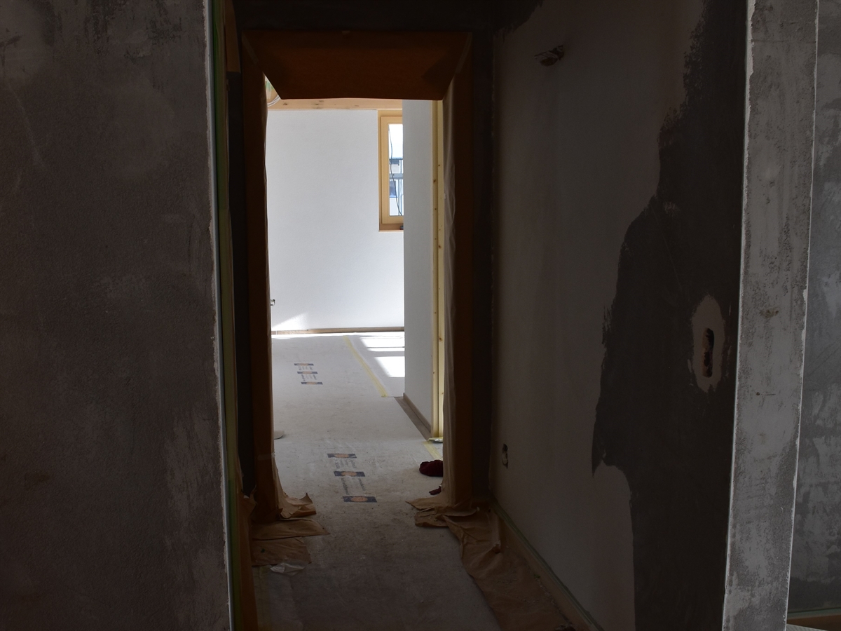 Der Innenbereich des Neubaus. Blick aus einem Gang auf eine abgeklebte Türzarge in den nächsten Raum.
