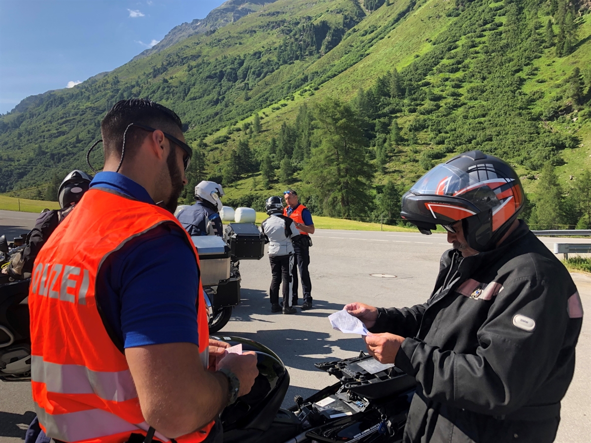 Zwei Polizisten unterhalten sich mit Motorradlenkenden auf einem Bündner Pass bei strahlend schönem Wetter
