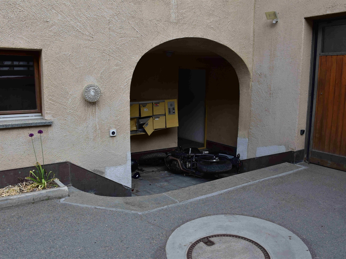Der leicht nach unten versetzte Eingangsbereich eines Hauses, in welchem das Motorrad am Boden liegt. Die Briefkästen sind teilweise beschädigt.