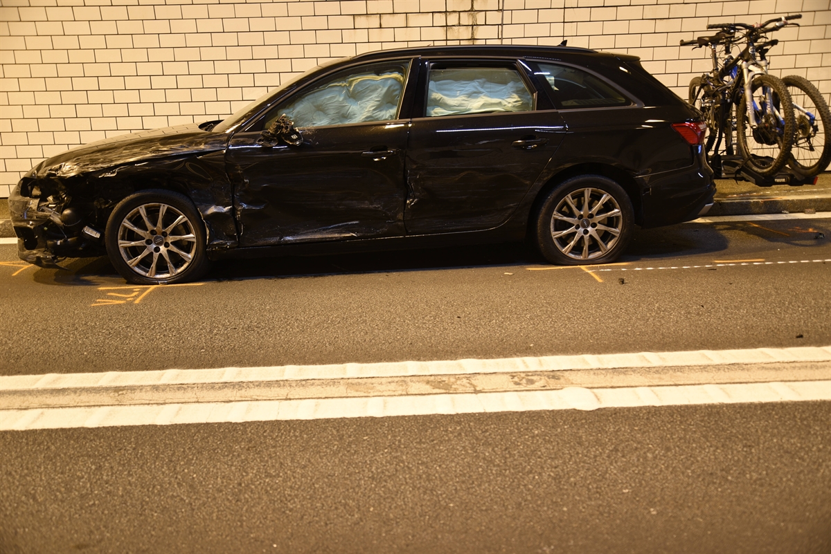 Schwarzes Auto im Seitenprofil beschädigt linke Seite und ein Veloträger mit zwei Velos. Airbags sind ausgelöst. Das Auto steht im Tunnel.