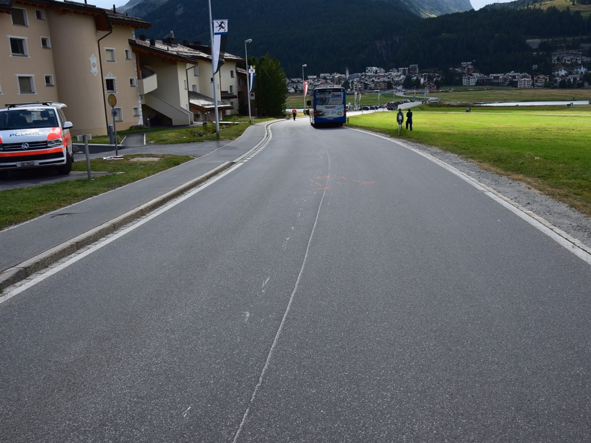 Auf der Via da Surlej steht der Linienbus. Links am Bildrand ein Patrouillenfahrzeug der Kantonspolizei Graubünden auf einem Platz.