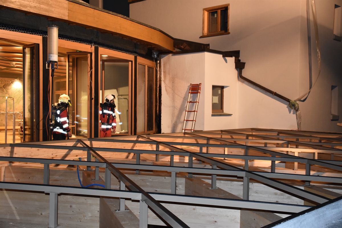 Zwei Feuerwehrleute auf dem Dach des Hoteleingangs, Stahlkonstruktion auf Holz sichtbar
