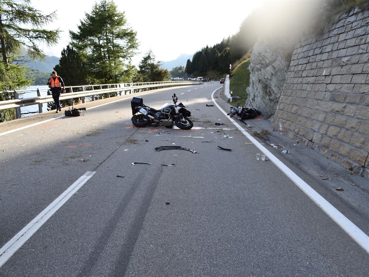 Zwei auf der Hauptstrasse am Boden liegende Motorräder. Im Hintergrund das Unfallauto. Links der Silsersee.