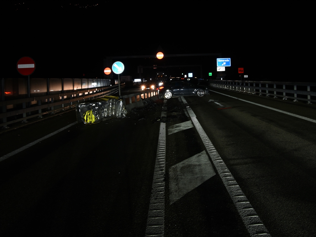 Nachtaufnahme welche diverse Signalisationen und Markierungen zeigt. Rechts der beschädigten Mittelleitplanke steht das dunkle Unfallauto quer auf der Fahrbahn.
