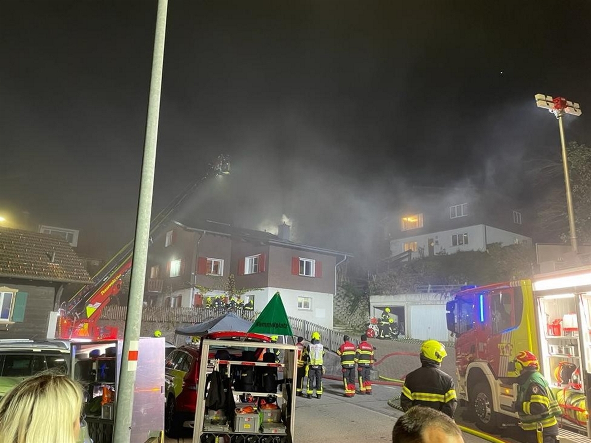 Fahrzeuge der Feuerwehr Chur stehen vor dem Zweifamilienhaus, aus welchem Rauch austritt. Über dem Dach befinden sich Feuerwehrleute auf einer Drehleiter.
